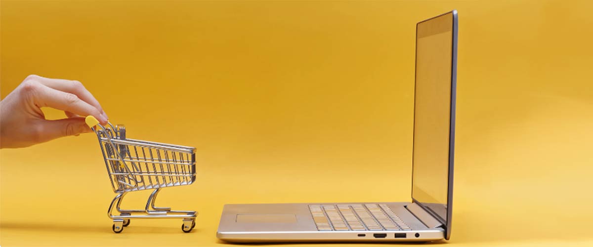 Man pushing a mini toy cart onto a laptop to signify Magento e-commerce sales